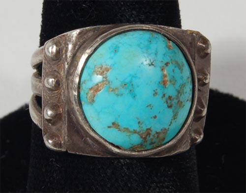 This exquisite ring is comprised of a wide shank that is split into 3 legs at the top of the ring that support a curved silver base on which rests this beautiful blue round and domed turquoise stone. Four silver rivets rest at the edges of the silver platform. The ring was made from heavy silver stock, possibly ingot silver and probably dates from the 1940s decade. It is in excellent condition.