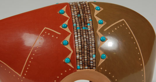 In this large pottery bear figurine, he applied a red slip to the front of the bear and a green slip to the rear.  Dividing the two colors are 7 rows of brown hieshe—dark brown in the center and lighter on the outer rows.  The hieshe is interspersed with a few beads of turquoise spread at intervals.  Small domed blue Kingman turquoise cabs are inserted in parallel rows framing the rows of hieshe.  A zigzag line goes from the mouth of the bear to the hind legs on each side.  Small dots outline these lines and outline the arch of the bear’s legs.