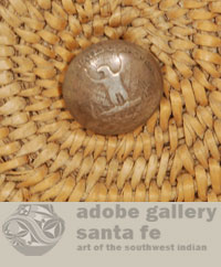 The hole in the center of the basket is traditionally filled with a piece of fabric to prevent sacred cornmeal from falling through during a ceremony.  A past owner has placed a button, made from a very old U. S. quarter coin, in the hole to permit hanging the basket on a wall.