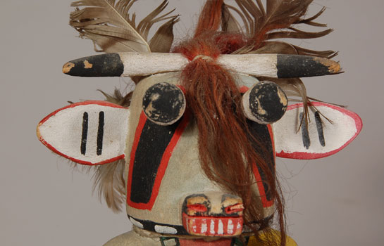 This Hopi Wakas (Cow) Katsina Doll is probably from the 1940s decade. He is constructed from cottonwood root and painted with casein and vegetal paints. He has a rattle in his right hand and a stick in his left. The traditional Hopi wide woven and embroidered sash hangs down his right side.  This Katsina seems to have first appeared in the Hopi pantheon of Katsinas around 1900 and has appeared regularly since then.