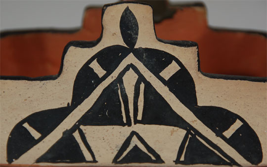 There is very little published information about the function or use of these rectangular pottery boxes. For sure, they were made long before pottery was being made to sell to non-Indians, so I do not believe that they were originally made as collectible boxes for tourists. The only instance when I have ever witnessed one in use was at the home of Helen and Fred Cordero of Cochiti Pueblo.  I went to the Cordero home very early one morning because I wanted Fred’s opinion concerning a jar I had recently acquired and which appeared to have been used as a pottery drum. I had to be back in Albuquerque early enough to open the gallery that day, so I struck out early to see him.  I arrived at the Cordero home just at sunrise. As I pulled the car up next to their house, I saw Fred standing at the doorway, with the screen door open, and he held a pottery box in his hand from which he was tossing cornmeal in the air toward the rising sun. I believe this to be a ritual performed at a thousand or more pueblo homes every morning.  Most of the earlier boxes had terraced rims, or as they are sometimes called, kiva step rims. I believe the terraces were eliminated in order to put lids on the boxes at some later date.  I don’t believe a lot of these were made for sale to tourists in the 1920s-1930s. A statement made by Ruth Bunzel in 1929 will help to clarify:   “Prices are conditioned by quality of craftsmanship and the fame of the maker….a small bowl of decorated black ware by Maria Martinez brings from three to six dollars. Large and unusual pieces, such as prayer bowls, vases, bring up to twelve dollars.”  Because they were doubled in price above the average bowl, I don’t expect the demand was great; therefore the supply would not have been great.  Also it must have been tempting to purchase a pot by Maria Martinez at half the price of other bowls.  This box has terrace rims on all four sides.  The terraces are included in the decoration of the side walls, providing extra surface for the design.    I suspect the box dates to the first quarter of the 20th century.  Condition: The tip of one terrace has been broken off and put back into place by native repair.  Provenance: from the collection of Katherine H. Rust 