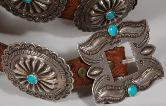 This fine old concha belt is chisel-stamped repoussé and filed.  Each of the 10 conchas features a sunburst at its dome capped with a single blue turquoise cab secured in a silver bezel.  The buckle is also of the same construction with two turquoise cabs.  This style is the epitome of the finest concha belts made in the mid-20th century.   The conchas are not overbearingly large and each is attached to the leather belt with a copper sleeve.    Silver jewelry from the early- to mid-20th century was still being produced by many Navajo at home in their hogans.  There was no widespread production by Natives working for outlets such as The Fred Harvey Company using company-supplied materials.  Belts such as this one were most certainly made by an individual silversmith and possibly sold to a trading post or dealer or an individual collector.  The early interest by tourists was a stimulus to fine craftsmanship.  It was only in the 1970s that quality gave way to quantity.  Condition:  the belt is in excellent condition  Provenance: from the collection of the Balcomb family  Recommended Reading: Indian Silver Jewelry of the Southwest 1868-1930 by Larry Frank Concho or Concha?  You will hear both words (we say conca), but they refer to the same thing.  Some history:  The word concho comes from the Spanish "concha" which actually means "conch" or "seashell" but has come to mean round, domed, or oval disks of silver used to decorate horse saddles or bridles and even on clothing.  It’s also seen as jewelry such as pendants, pins and even bolo ties.  What is most striking is when it’s seen adorning leather belts.  Perhaps you will even hear a single “concha” referred to as concha instead of concho. Concho belts are a long-time Navajo tradition yet it has been suggested (unknown source) that the Navajo borrowed conchos from Mexican tack items or from the Plains Indians.  The earliest conchos were silver dollars (coin silver) that were hammered, then stamped and edged, then slotted and strung together on a piece of leather.  Eventually, copper loops were added to the back of the conchos so that the conchos could be slipped onto a leather belt. Features of a Concho Belt: Concho belts can be a continuous row of conchos or could have spacers in between the conchos. The spacers can of various shapes but traditionally are butterflies and it is easy to see why they are called that when you look at the shape of them. The conchos and the butterflies are sometimes backed by leather which highlights the silver work and also protects the edges of the silver from bumping, wear or bending. Can a man or a woman wear a concho belt?   Concho belts are unisex and can be worn with jeans as well as dresses.  It is very “Santa Fe” to add a concho belt to your attire and can even be included with any clothing that is black in color.  When this is done, this creates what is considered “Santa Fe Formal” wear and is usually very stunning.  This approach really draws attention to the wearer’s concho belt and oftentimes, great conversation.   