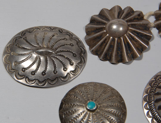 This group of seven silver buttons and concha came from the Balcomb family that owned a gallery in Gallup, New Mexico, and later in Albuquerque.  Mrs. Balcomb retired and closed the Albuquerque gallery in 1976.  These buttons were most likely in the earlier gallery in Gallup, the heart of Navajo Indian country.  Three of the buttons are fluted and measure 1-3/8 inch in diameter each.  Two of the buttons are stamped and measure 1-9/16 inch in diameter each.  The single button with a turquoise cab is stamped and measures 1-1/4 inch in diameter.  The oval silver one is a concha with a copper strap on verso through which a leather belt could be threaded.  It measures 1-9/16 inch x 1-3/4 inch.  Condition:  all are in original condition  Provenance:  from the Balcomb family 