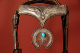 When the Spaniards introduced horses to the Navajo, it gave them mobility to plunder and raid their neighbors.  They rapidly became a semi-nomadic people and lavished beautiful blankets and silver on their horses, much like the Plains Indians did with beadwork.  Their lifestyle paralleled that of another nomadic peoples who lived in deserts and treasured their horses—the Arabs.  This is an early 20th century Navajo headstall with stamped and punched conchas on either side of a beautiful centerpiece with repoussé design and with a silver naja suspended from it.  The leather terminal connectors, which join the headstall to the bit, are encased in beautifully-stamped silver designs.  The leather quirt is beautifully woven from leather strips in a fashion not knowingly by Navajo artists.  This style work is not known in their culture.  It is quite possible that it was a trade item to which the owner added turquoise to match the headstall.  Both the headstall and quirt have been mounted on metal stands for display purposes.  The sterling silver items on the headstall have not been polished in the 45 years that the headstall has been owned by the current owner.  We have chosen to leave the silver unpolished because it helps illustrate the age of the item and some collectors prefer that all patina remain untouched.  Condition: both headstall and quirt are in excellent condition  Provenance: from a New York City collector  Recommended Reading:  Indian Silver Jewelry of the Southwest 1868-1930 by Larry Frank 