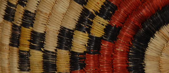 Coiled basketry of this type is made exclusively in Second Mesa villages on the Hopi Reservation. Each stitch of a coil is interlocked into the adjoining stitch of the previous coil. An awl is used to facilitate this. This basket probably took the weaver more than two months to complete the weaving process alone, not counting the months of gathering materials, drying the yucca leaves, then splitting them to a thin, consistent width, dying some of them, and preparing the grass for the foundation. I have watched a number of women at Second Mesa villages make baskets over the years, and I am in awe of their patience and fortitude.  The design of this plaque is very subtlety divided into four quadrants by a very faint green pigment applied over the yucca, a technique I have not seen before on Hopi basketry.  The two large designs with red appear to possibly represent an unmarried Hopi girl’s hair whorl, but this is speculation on our part. It is conceivable that this was used in a ceremonial function relating to a young Hopi female.  Condition:  very slight fading between front and back, otherwise in excellent condition Provenance: from the collection of a member of the Balcomb family Recommended Reading:  Hopi Basket Weaving, Artistry in Natural Fibers, by Helga Teiwes. 