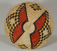 Coiled basketry of this type is made exclusively in Second Mesa villages on the Hopi Reservation. Each stitch of a coil is interlocked into the adjoining stitch of the previous coil. An awl is used to facilitate this. This basket probably took the weaver more than two months to complete the weaving process alone, not counting the months of gathering materials, drying the yucca leaves, then splitting them to a thin, consistent width, dying some of them, and preparing the grass for the foundation. I have watched a number of women at Second Mesa villages make baskets over the years, and I am in awe of their patience and fortitude.   The design of this plaque is very subtlety divided into four quadrants by a very faint green pigment applied over the yucca, a technique I have not seen before on Hopi basketry.  The two large designs with red appear to possibly represent an unmarried Hopi girl's hair whorl, but this is speculation on our part. It is conceivable that this was used in a ceremonial function relating to a young Hopi female.   Condition:  very slight fading between front and back, otherwise in excellent condition Provenance: from the collection of a member of the Balcomb family Recommended Reading:  Hopi Basket Weaving, Artistry in Natural Fibers, by Helga Teiwes.