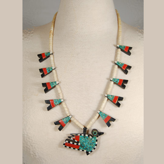 This necklace was made from several "found materials." The beads were made from bone, the black backing probably from automotive battery casing, the red from toothbrush handles or something similar, and the turquoise is genuine. These necklaces were usually in the squash blossom style, with pendants protruding from the sides and a bird pendant at the bottom, as is this one.   Most necklaces of this style have a pendant bird in the shape of the mythical thunderbird, a squared-off bird facing full forward.  This necklace features a more realistic Kewa-style bird as seen on that pueblo's pottery-a much rarer style of pendant.   During the 1930s when the Depression-era was in full swing, New Mexico Pueblo Indians were severely affected. At Santo Domingo Pueblo (now Kewa Pueblo), the Indians became very resourceful and began producing jewelry from whatever materials they could find. One particular folk art creation they produced has become a very collectible item: the Depression-era necklace.  Production continued at a lesser rate into the mid-20th century.   Condition:  very good condition Provenance: from the personal collection of Margaret Gutierrez of Santa Clara Pueblo Recommended Reading: "Santo Domingo Pueblo Jewelry" by Sally and J. Roderick Moore in The Magazine Antiques, Brant Publications, Inc. July 2009, vol. CLXXVI, no. 1. pp. 56-61