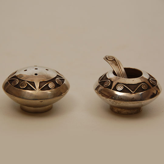 This set consists of a sterling silver salt cellar and serving spoon and a pepper shaker, all in the style of Navajo, or quite possibly Hopi silverwork.  The workmanship is extraordinary with a top layer consisting of cutout designs imposed over a lower layer of smoke-colored silver backing. It is the overlay technique that makes us say it could be of Hopi origin.   Condition: original condition Provenance: from the personal collection of Margaret Gutierrez, Santa Clara Pueblo Recommended Reading: Masterworks and Eccentricities: The Druckman Collection; Navajo and Pueblo Jewelry and Metalwork 1880-1950 by Robert Bauver