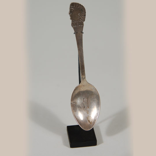 Navajo-made silver spoons with an Indian head profile at the end of the handle first appeared in Indian trader J. L. Hubbell's 1902 pamphlet.  Hubbell assured his clients that these were made by Navajo silversmiths and were made from coin silver.    This spoon features an Indian head with feather bonnet in profile at the end of the handle and two arrows stamped in the bowl.  Spoons were priced by weight of silver and not by their aesthetics.  Spoons such as these were highly sought by tourists traveling on the trains to the southwest.  They were attractive items, easily transported and easily displayed when back at home.   This spoon comes with a metal display stand fabricated specifically for this item.   Condition:  there is a small crack on one edge of the bowl and the handle may have been repaired near the area of the bowl of this spoon. Provenance:  Coulter Brooks Gallery, Santa Fe                          private collection of a Virginia family Recommended Reading; Navajo Spoons: Indian Artistry and the Souvenir Trade, 1880s - 1940s by Cindra Kline