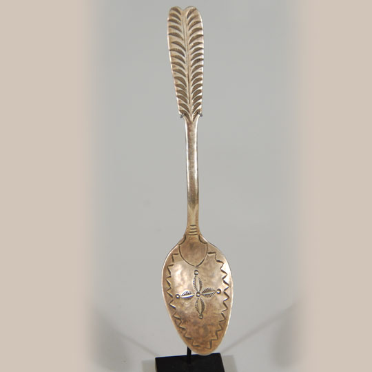 This elaborately decorated silver spoon features a feather-pattern handle and a stamped bowl of elaborate symbols.  It dates to circa 1900.  Spoons such as this appeared in pamphlets and catalogs of Navajo traders as early as 1902 and possibly earlier.  Traders such as Lorenzo Hubbell, C. N. Cotton, and J. B. Moore featured them.  Moore advertised them at $1.50 per oz.   The fascination with Navajo-made silver spoons waned around 1915.  Navajo smiths switched from making souvenir spoons to making, on special order, complete table service silver.   This spoon comes with a specially-made display stand that permits the spoon to be displayed in a frontal view.    Condition: original condition Provenance:  Medicine Man Gallery, Santa Fe                       private Virginia family collection Recommended Reading; Navajo Spoons: Indian Artistry and the Souvenir Trade, 1880s - 1940s by Cindra Kline