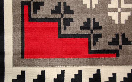 Close up view - Patterns associated with weavers from the Klagetoh area consist of a large diamond in the center of the textile surrounded by a border or borders of stepped and hook designs.