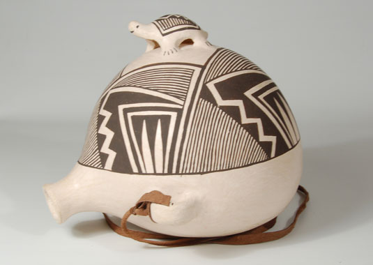 This canteen was made to sit at a slight angle, leaning toward the back, so the entire face design would be visible.  The design is a contemporary adaptation of a prehistoric one.  It is arranged so as to provide a frame for the appliqué turtle figure attached to the apex of the body.  The design on the shell of the turtle is coordinated with that on the canteen.  