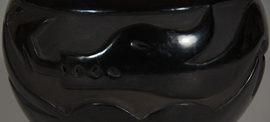 The design is a traditional Avanyu realized by carving out the clay surrounding the serpent.  Below the Avanyu are waves reflecting water in which the water serpent resides.  