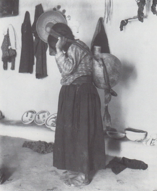 “Nampeyo carrying an olla/” Adam Clark Vroman, 1901.  (The Southwest Museum, Los Angeles.  Photo #N22764.)  Nampeyo posed for Vroman inside her home with a typical canteen carried by women to carry water from the spring below the mesa.